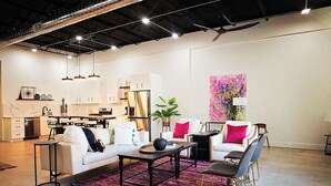 A modern living room with a white sofa, a coffee table, and a colorful rug. There is a kitchen area with white cabinets and a dining table. - Frida's House - Historic Downtown  (San Angelo)