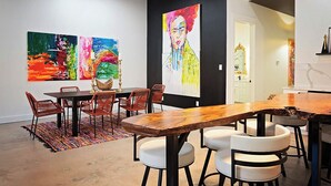 An art gallery with a wooden table and chairs, surrounded by colorful paintings. - Frida's House - Historic Downtown  (San Angelo)