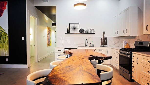 A modern kitchen with a long wooden table, white cabinets, and a black stove. - Frida's House - Historic Downtown  (San Angelo)