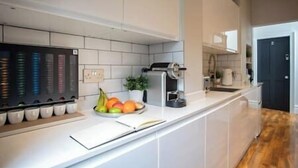 A modern kitchen with white cabinets, a coffee machine, and a fruit bowl on the counter. - Cosy King Suite close to Manchester City Centre, Room 2 (Stockport)