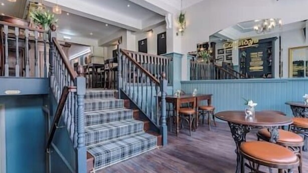 A spacious interior with a wooden staircase, a dining area with round tables and chairs, and a bar area with a blue wall. - Cosy King Suite close to Manchester City Centre, Room 2 (Stockport)