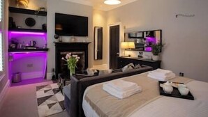 A modern hotel room with a bed, bedside table, lamp, and a flat-screen TV mounted on the wall. - Cosy King Suite close to Manchester City Centre, Room 2 (Stockport)