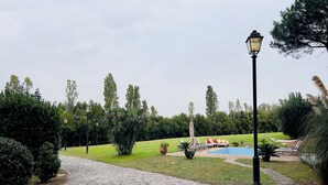 Un chemin pavé mène à un espace piscine agrémenté de chaises longues et d’une statue.