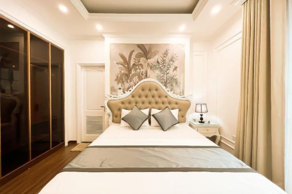 A bedroom with a tufted headboard, a large bed with grey bedding, a nightstand with a lamp, and a sliding door closet.