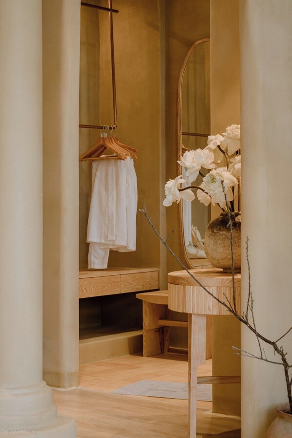 A bathroom with a wooden vanity, a hanging towel rack, a mirror, and a vase with white flowers. - Phoenix Villas Sun Ha Long (Bai Chay)