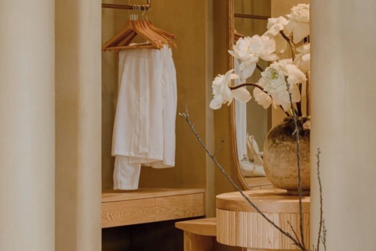 Un baño con tocador de madera, un perchero para toallas y un florero con flores blancas.
