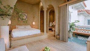 Een slaapkamer met een bed, een houten bankje, een potplant en uitzicht op het balkon.