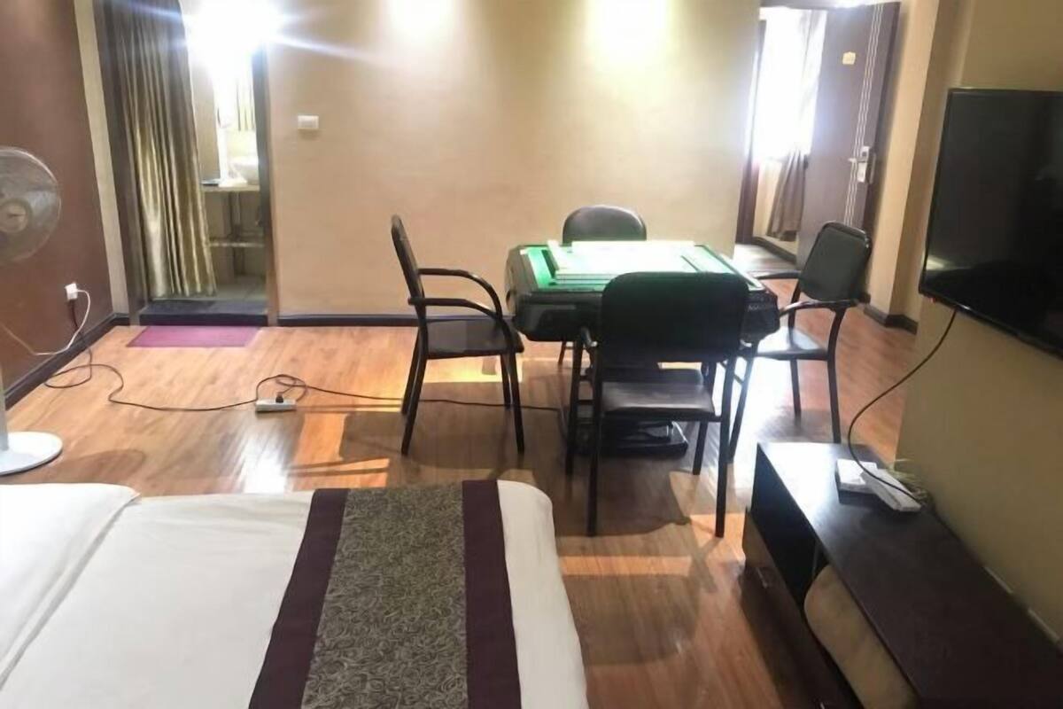 A hotel room with a bed, a desk with a chair, a television, and a fan.