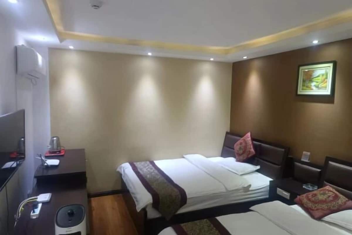 A hotel room with two beds, a desk with a computer, a chair, and a small table with a lamp.