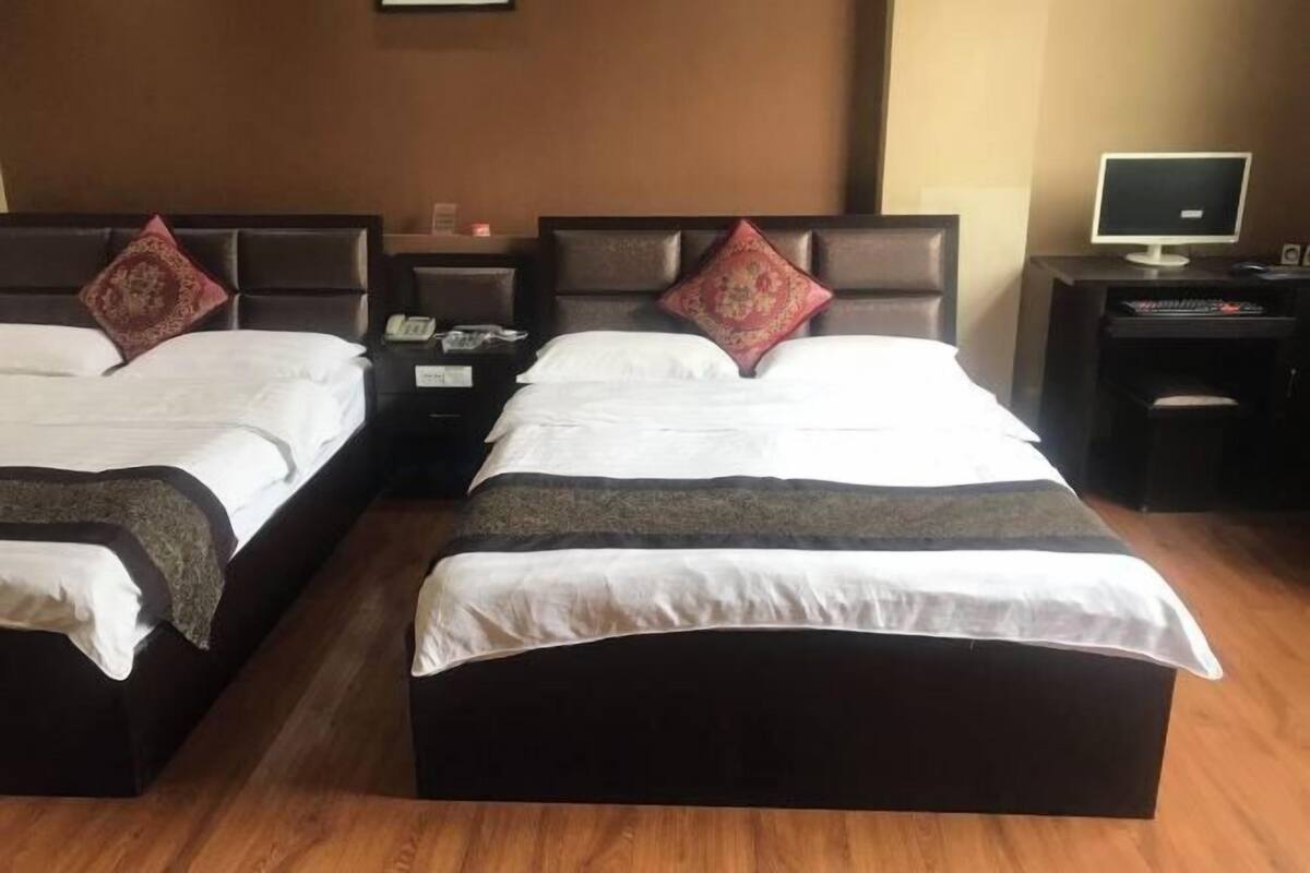 A hotel room with two beds, each with a headboard, bedside tables, and a television on a stand.