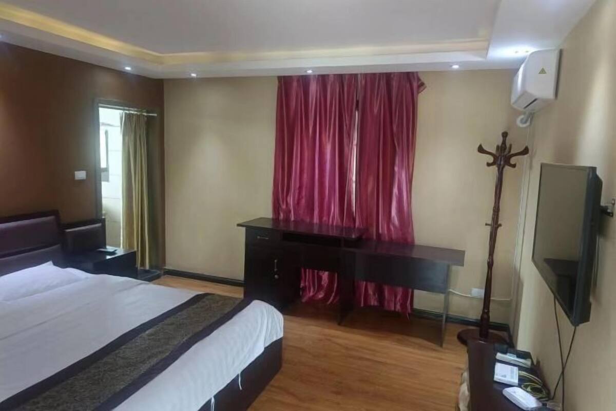 A hotel room with a bed, a desk, a coat rack, and a TV.