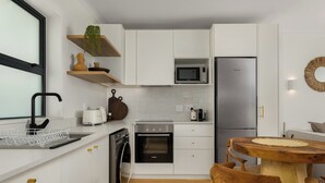A modern kitchen with white cabinets, a stainless steel refrigerator, a microwave, and a wooden dining table.