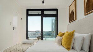 A modern hotel room with a large bed, a view of the city through a glass door, and a cityscape visible outside.