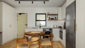 A modern kitchen with white cabinets, a built-in oven, a stainless steel refrigerator, and a round wooden table with two chairs.
