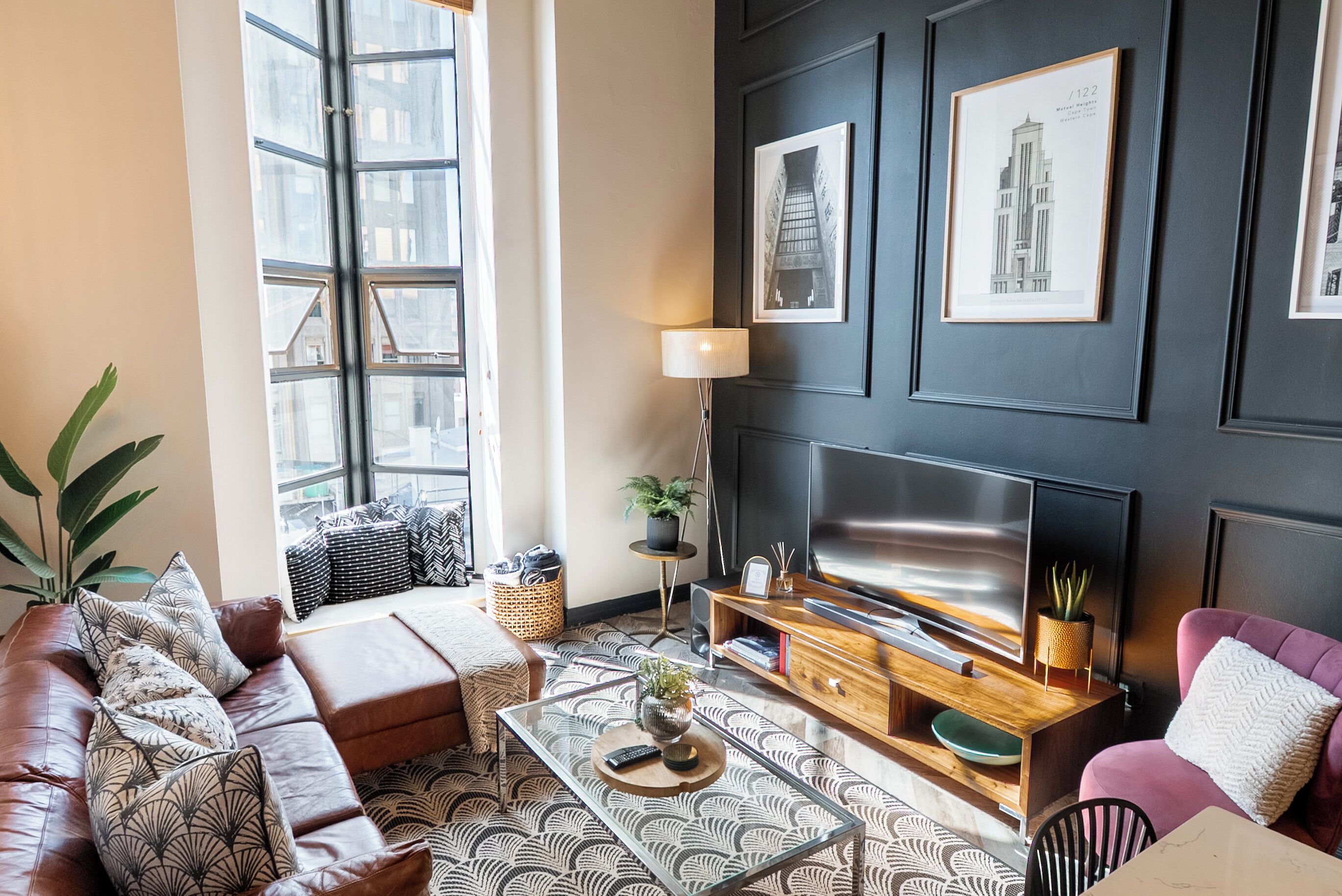 A modern living room with a leather sofa, a glass coffee table, a flat-screen TV, and framed artwork on the wall.