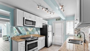 A modern kitchen with white cabinets, a granite countertop, stainless steel appliances, and a window with blinds. - Mermaid’s Retreat - Heated Private Pool, Walk to Beach, Complimentary Bikes! (Santa Rosa Beach)