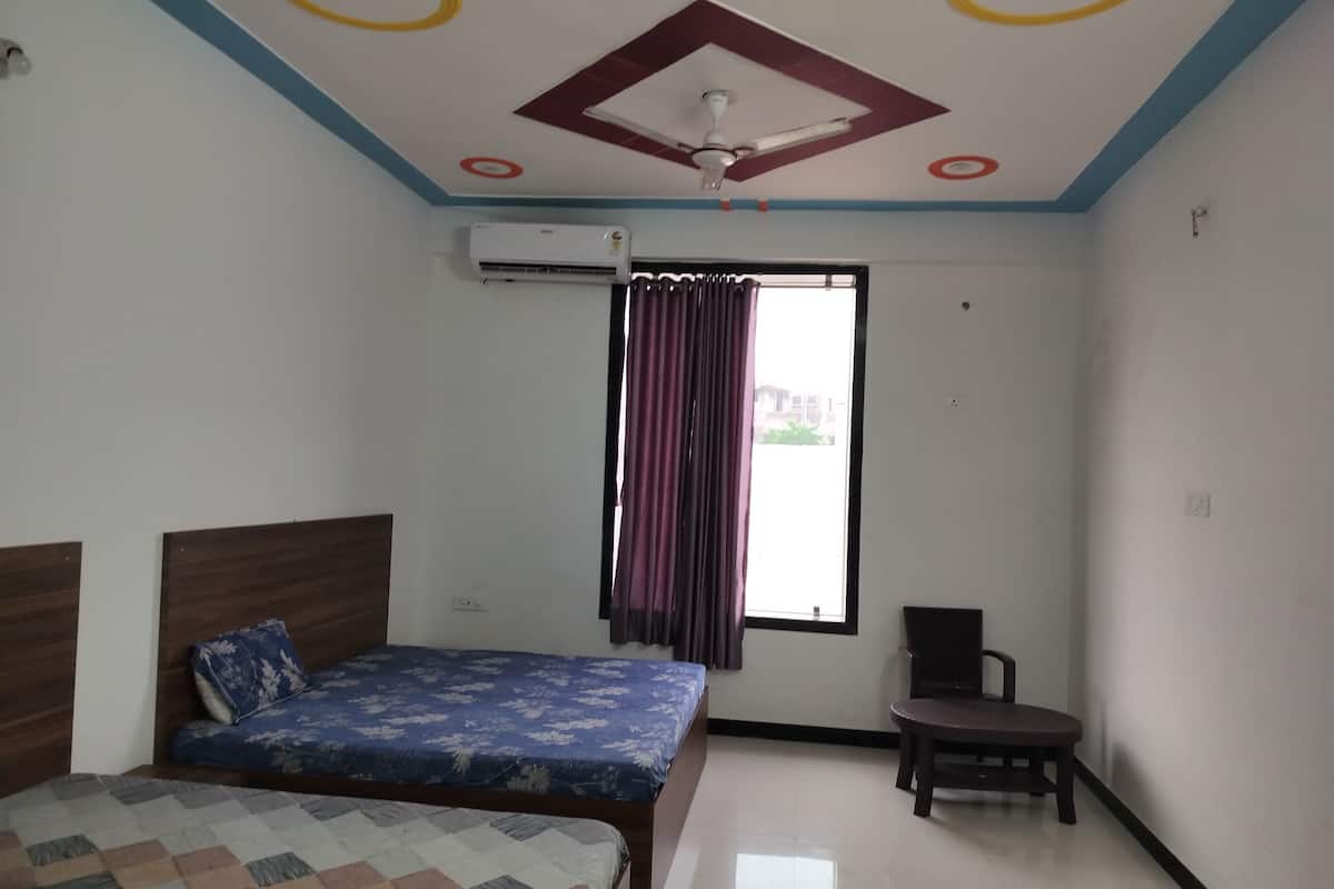 A bedroom with a bed, a chair, an air conditioning unit, a window with curtains, and a ceiling fan.