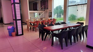 Comedor con varias mesas y sillas, una escalera y grandes ventanales.