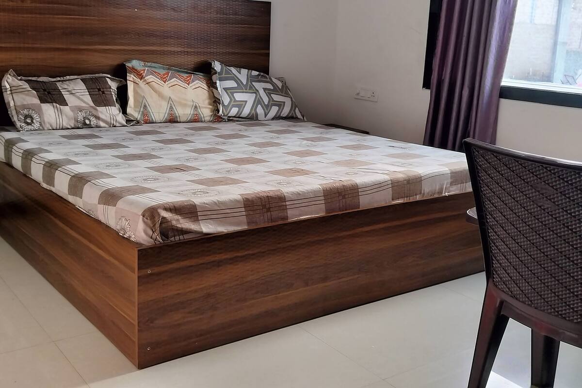 A bed with a patterned bedspread and multiple pillows, a wooden headboard, and a chair with a textured backrest.