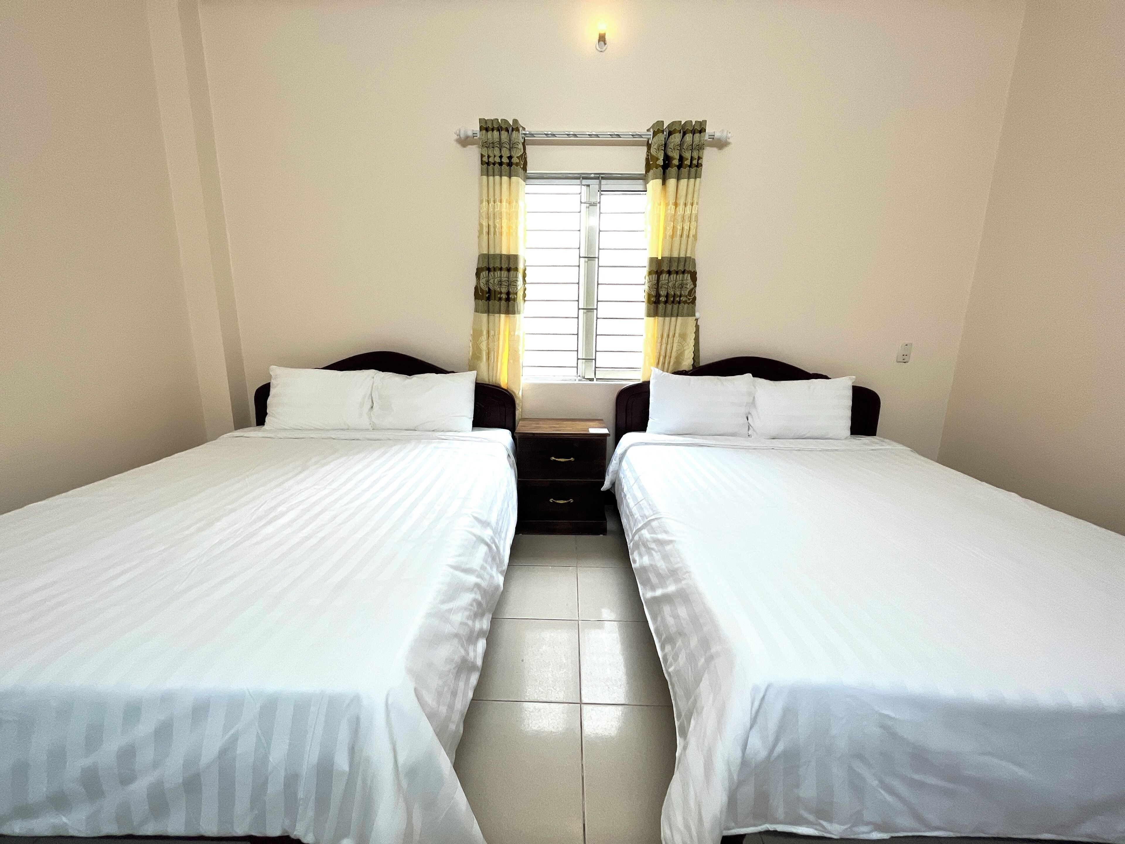 A room with two single beds, a window with curtains, and a light fixture on the wall.