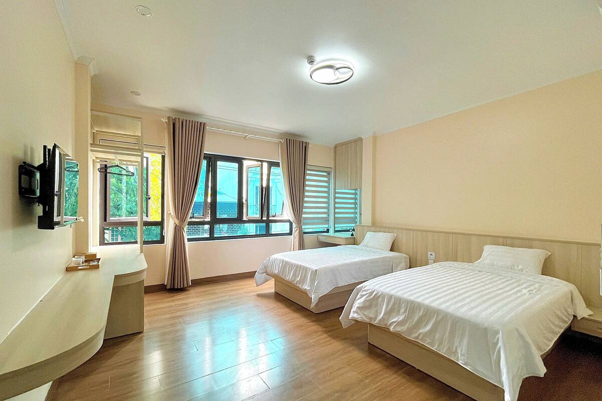 Una habitación de hotel con dos camas, un televisor montado en la pared, un escritorio y una ventana con cortinas.