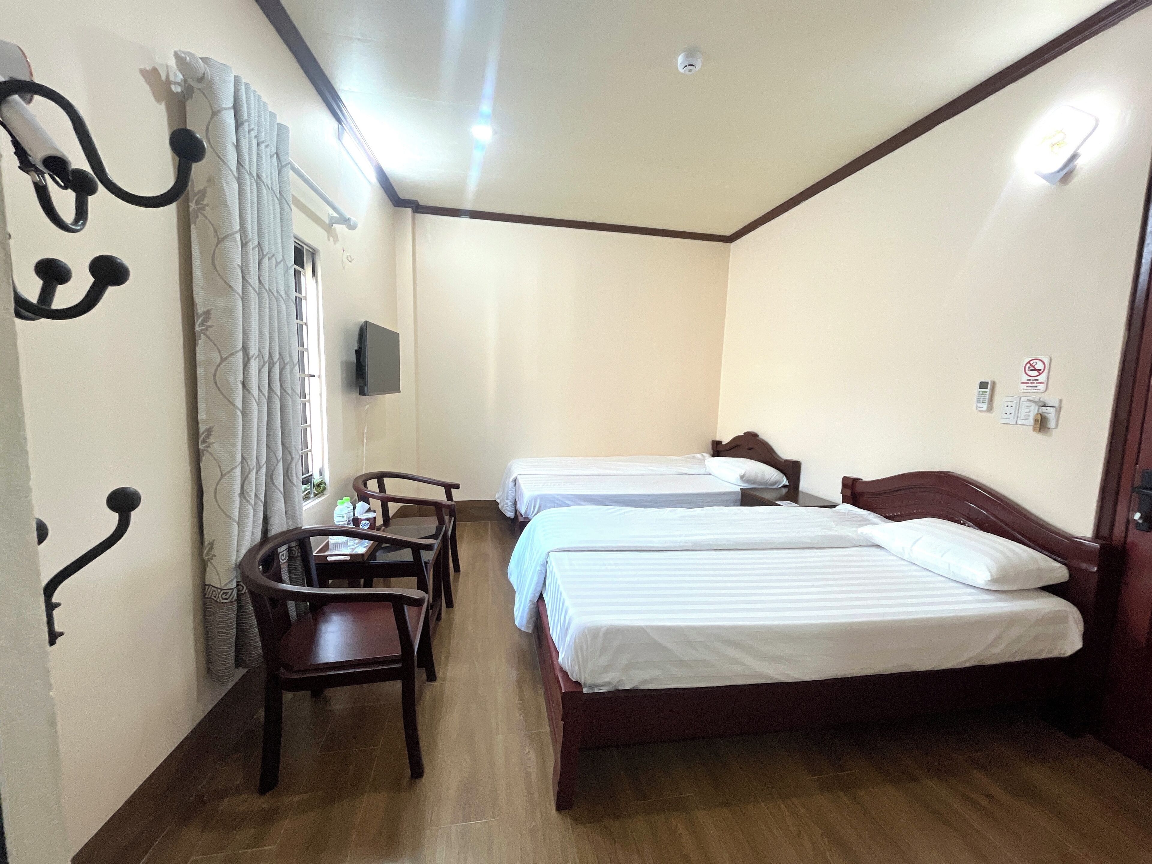 Quarto de hotel com duas camas, uma mesa, uma cadeira, uma TV e uma janela com cortinas.
