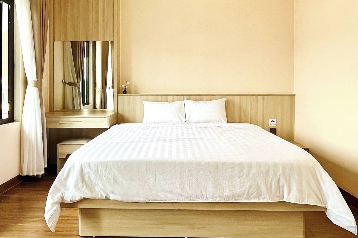 Una habitación de hotel con una cama grande, una mesita de noche, un espejo y una ventana con cortinas.
