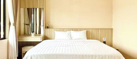 Quarto de hotel com uma cama grande, uma mesa de cabeceira, um espelho e uma janela com cortinas.