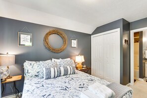 Une chambre à coucher avec un lit, deux tables de chevet avec des lampes, un miroir fixé au mur et une porte.