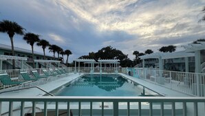 Un área de piscina con sillones reclinables, una zona de estar cubierta y vistas de los edificios circundantes.