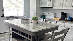 Una cocina con isla central, armarios blancos, un microondas y una tetera.