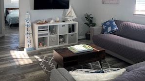 Una sala de estar moderna con un sofá gris, una mesa de centro, un televisor, un ventilador de techo y una estantería.