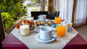 Aamiaispöydällä on croissantteja, maitoa, muroja, appelsiinimehua ja kuppi.