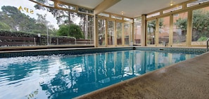 An indoor swimming pool with clear glass walls, surrounded by a tiled border and a wooden deck. - Piedras Doradas (Valeria del Mar)