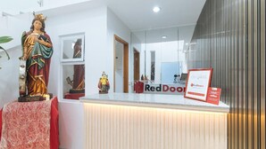 A reception desk with a statue of Saint Catherine of Alexandria, a RedDoorz sign, and a mirror reflecting the interior. - Reddoorz @ St. Catherine Residences Olongapo City (Olongapo)