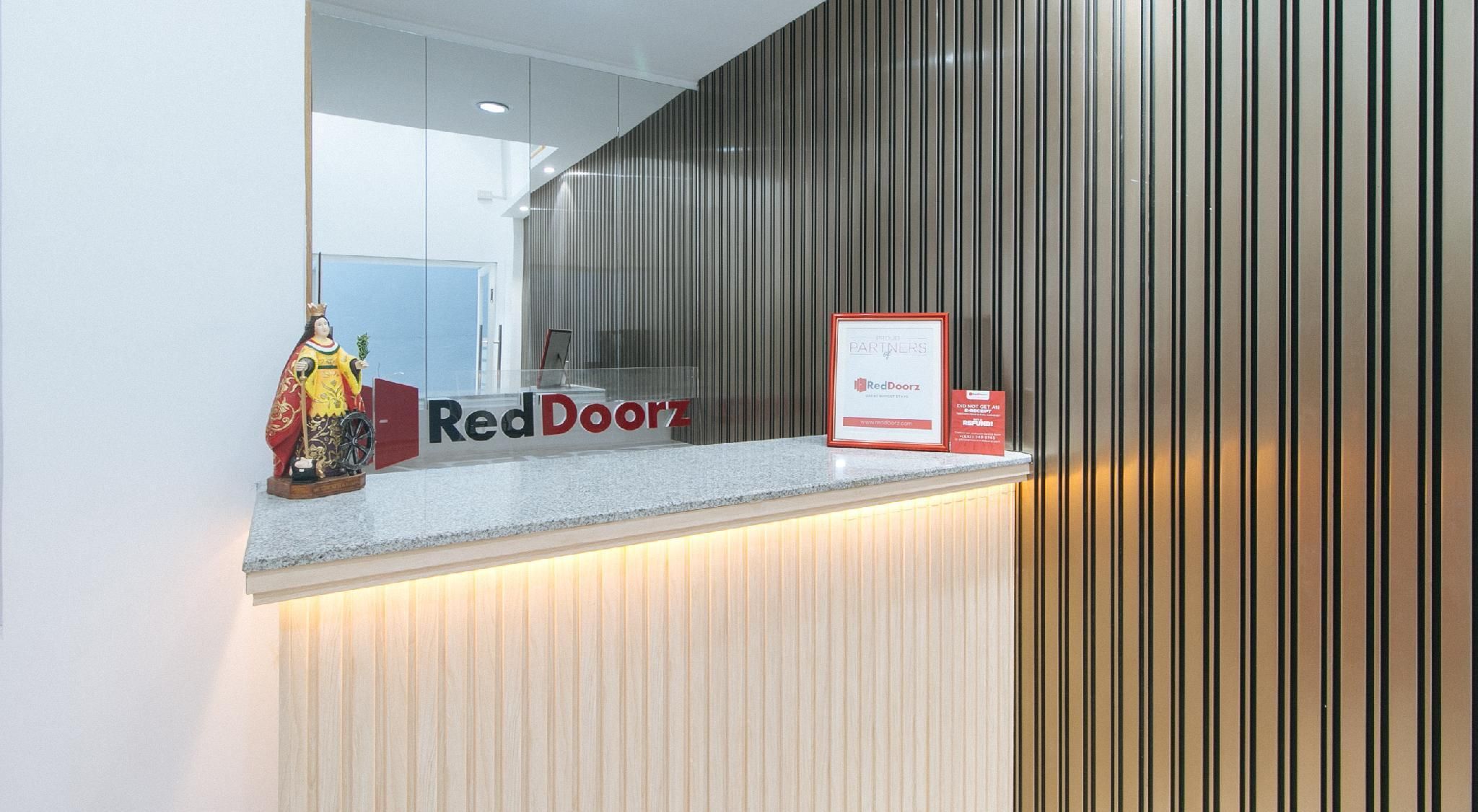 A reception desk with a RedDoorz sign, a framed notice, and a statue.