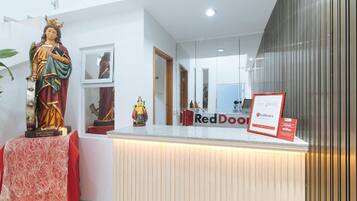 A reception desk with a statue of Saint Catherine of Alexandria, a RedDoorz sign, and a mirror reflecting the interior.