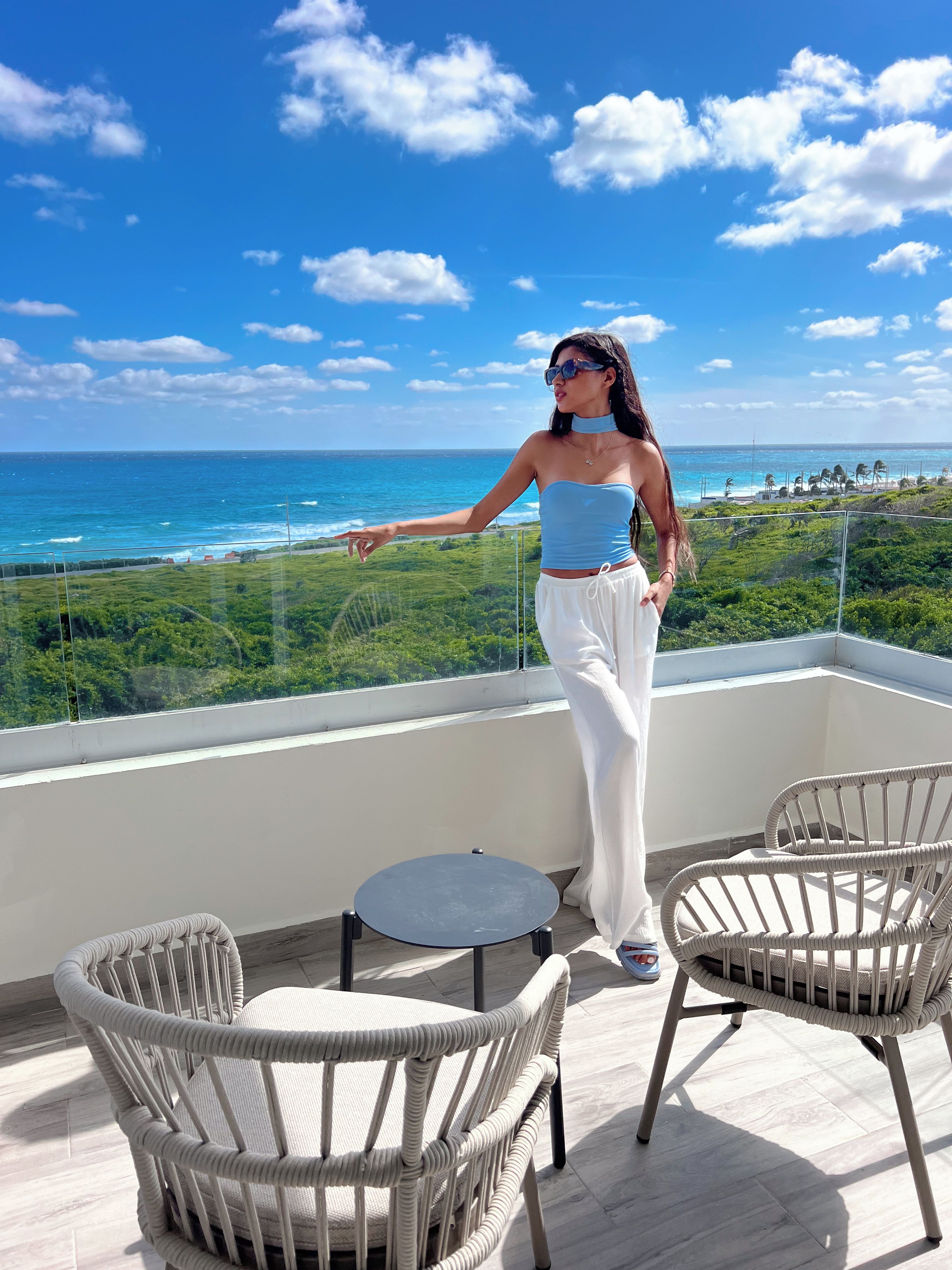 A balcony with a view of the ocean, two wicker chairs, and a small round table.