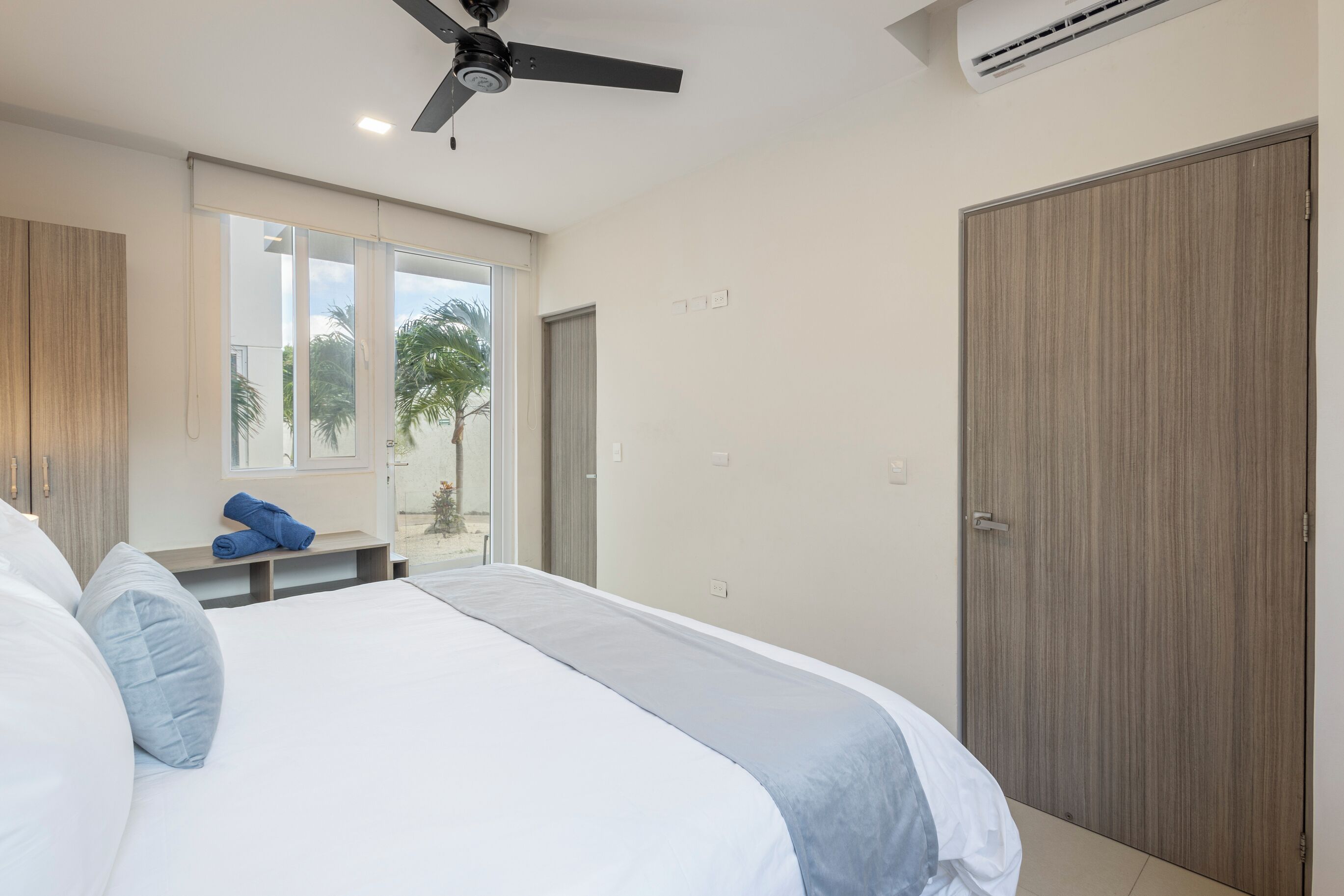 A bedroom with a bed, a ceiling fan, a window, a door, and an air conditioning unit.