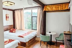 Ein Hotelzimmer mit einem Bett, zwei Stühlen, einem kleinen Tisch und einem Fenster mit Vorhängen.