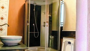 Une douche d’angle avec un pare-douche en verre, un lavabo blanc avec un récipient à rayures bleues et des toilettes blanches.