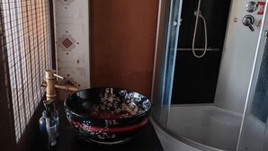 Une salle de bain avec un espace douche, un lavabo noir orné de motifs floraux et un robinet.