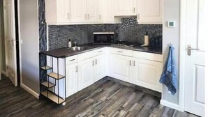 Une cuisine de taille réduite avec des meubles blancs, un dosseret en carreaux noirs et un plancher en bois.