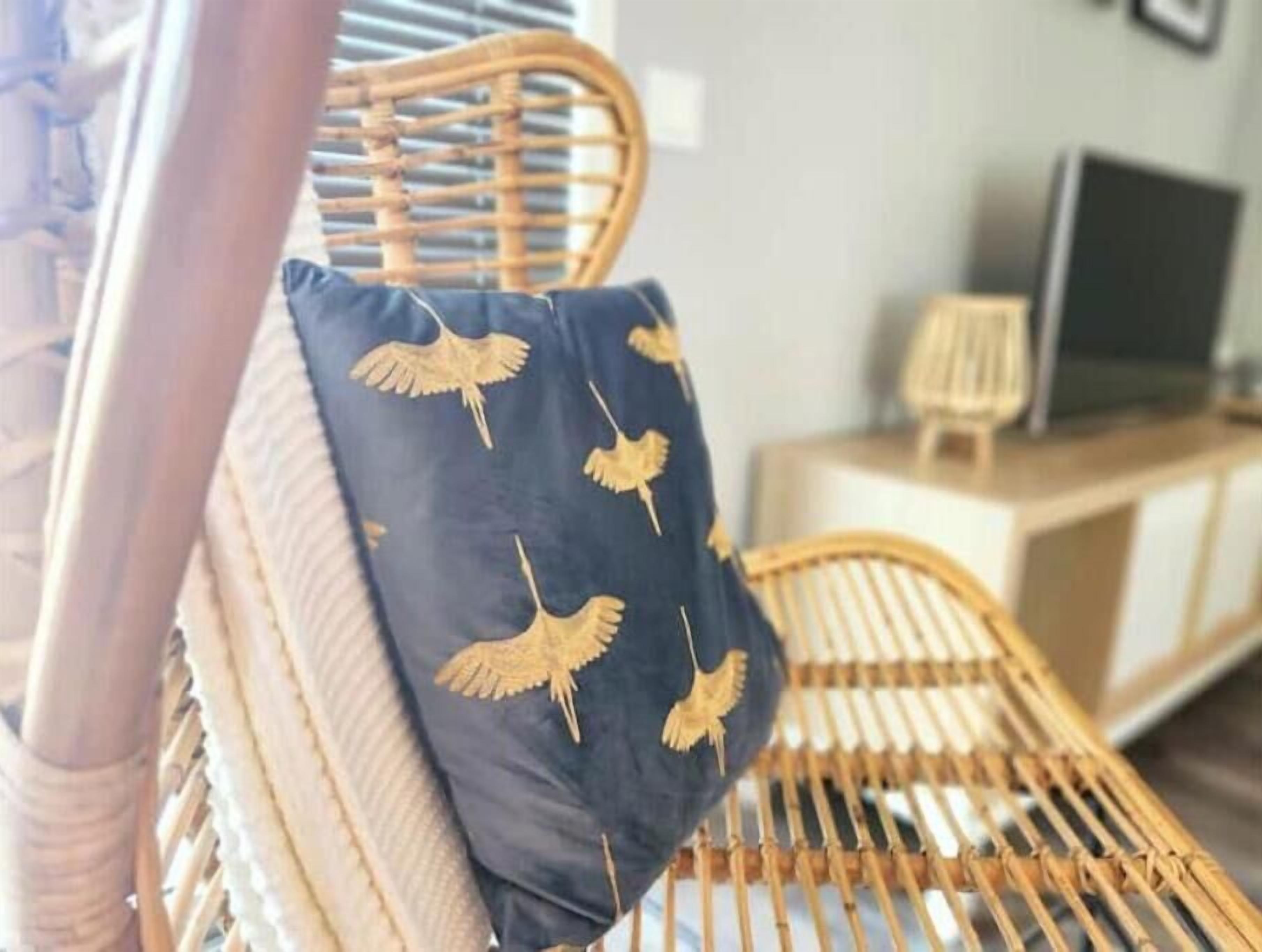 Ein Korbstuhl mit dunkler Sitzkissen, verziert mit goldenen Vogelmotiven.