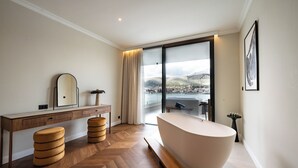 Ein modernes Badezimmer mit einer großen Badewanne, Holzboden und Blick auf eine Stadtlandschaft durch große Fenster.