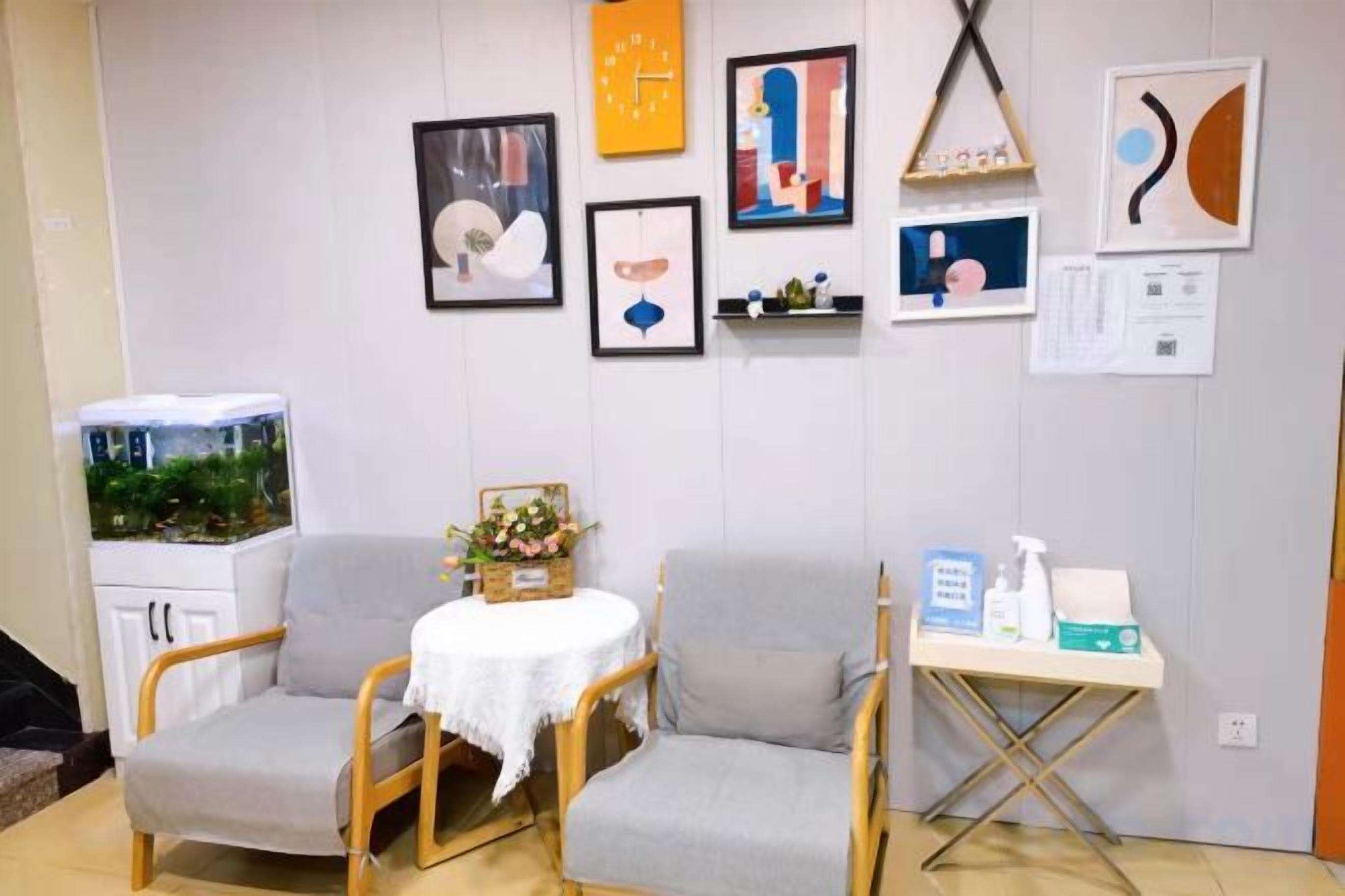 Una habitación con dos sillones grises, una mesita con mantel blanco y una estantería con diversos objetos.