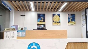 A reception desk with a wooden finish, a blue logo, and three framed artworks depicting deer and trees. - Nanwang Hotel (Shanghai Fengxian University Town) (Shanghai)