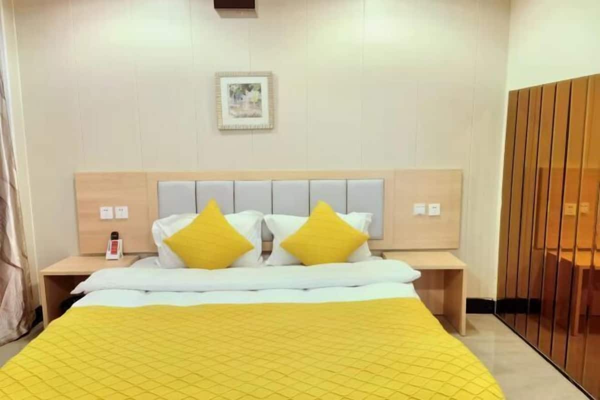 A hotel room with a bed, two bedside tables, a bedside lamp, a wooden headboard, and a wardrobe.