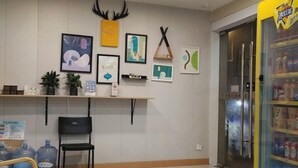 A reception area with a desk, chairs, framed artwork, a clock, and a refrigerator. - Nanwang Hotel (Shanghai Fengxian University Town) (Shanghai)