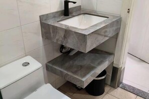 Ein Badezimmer mit einer weißen Toilette, einem Waschbecken mit einem schwarzen Wasserhahn und einem Mülleimer.